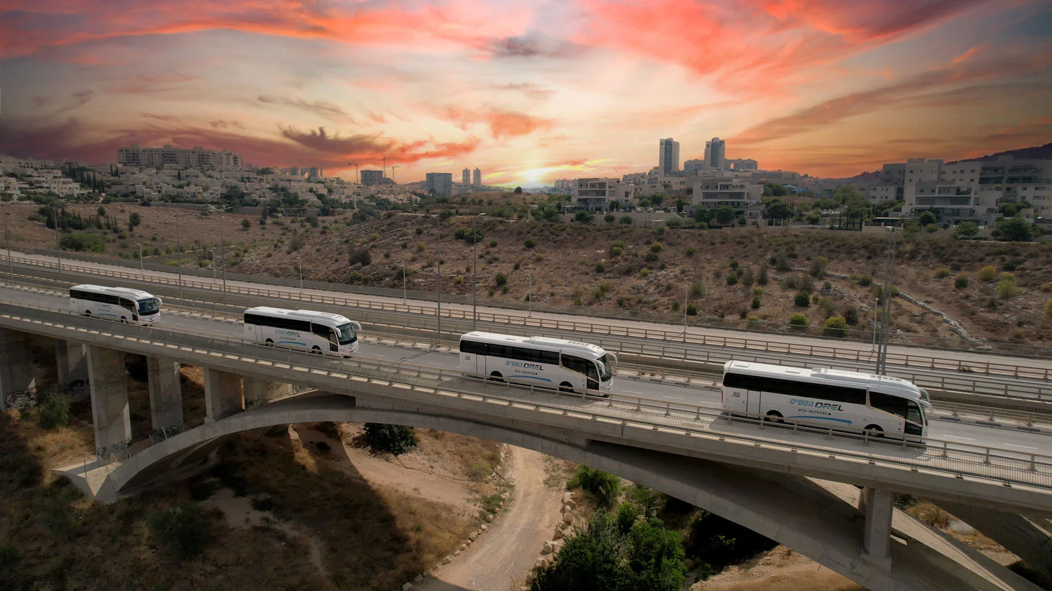 צי האוטובוסים של אוראל הסעים על גשר בשעת שקיעה